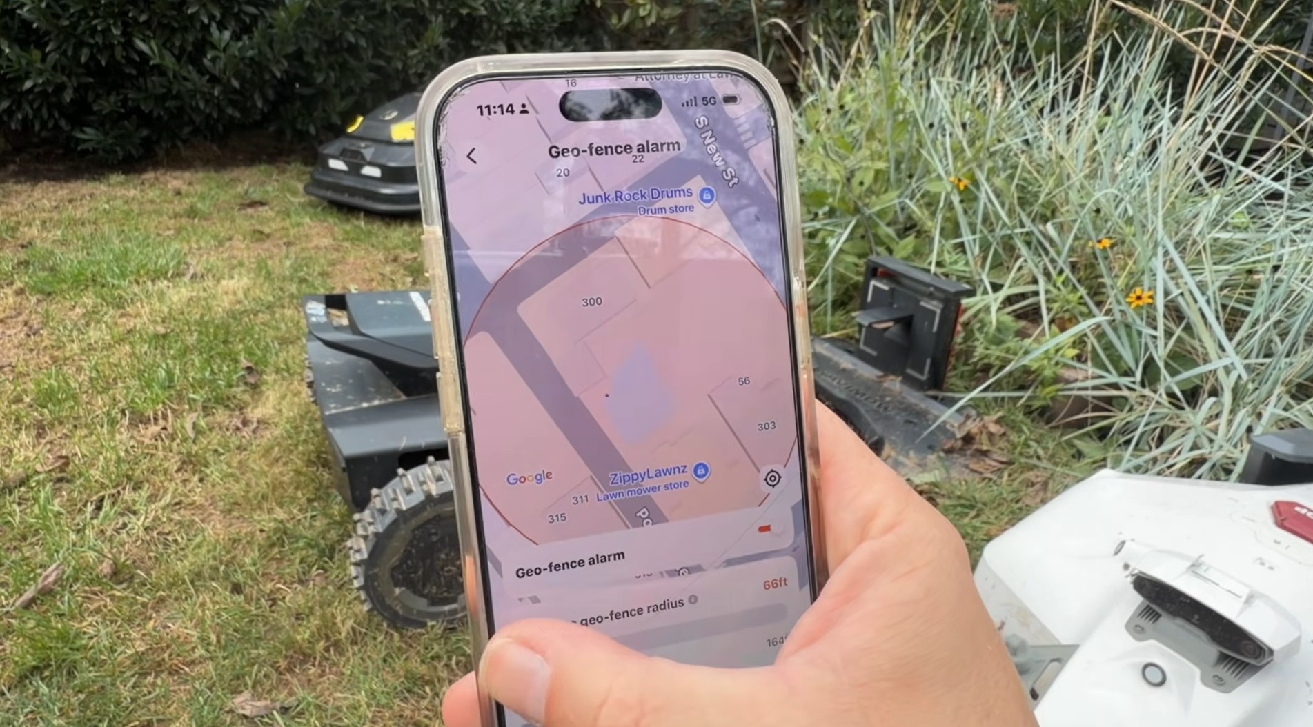 The Navimow app's geo-fence alarm screen showing a radius drawn around the Zippy Lawnz store, with Navimow mowers on the lawn behind the phone