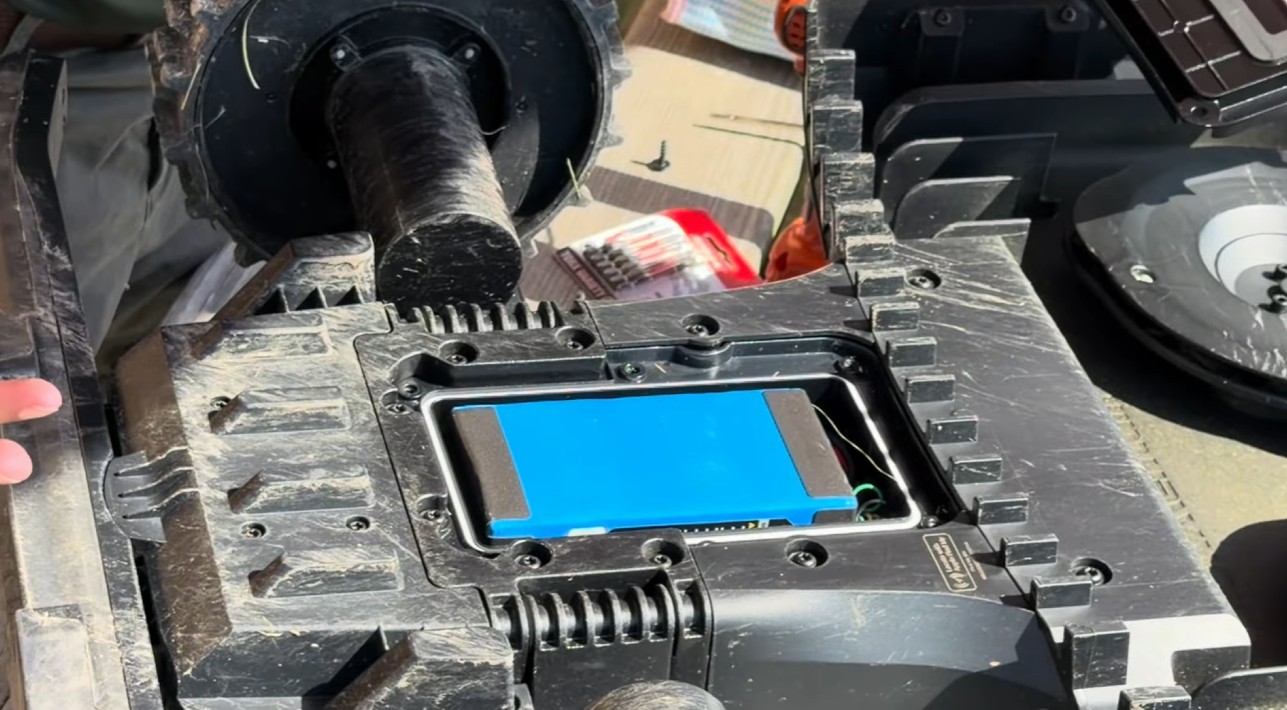 A blue lithium-ion battery pack seated in the chassis of a robot mower with the protective cover removed