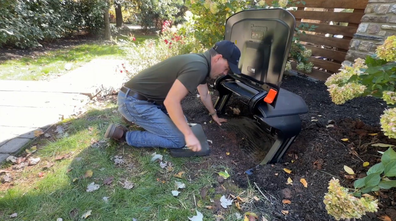 A Zippy Lawnz installer setting a Navimow garage over the charging station in a mulch bed at a Phoenixville, PA home