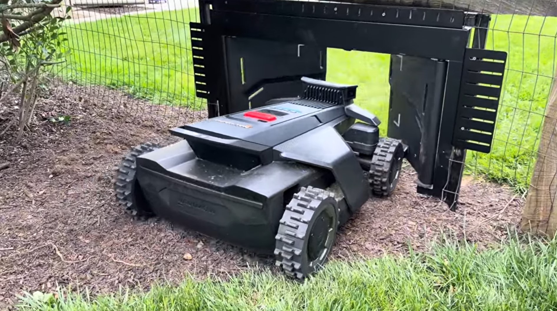 A Navimow mower driving out of a MowGate installed in a welded-wire fence with side brackets and supports