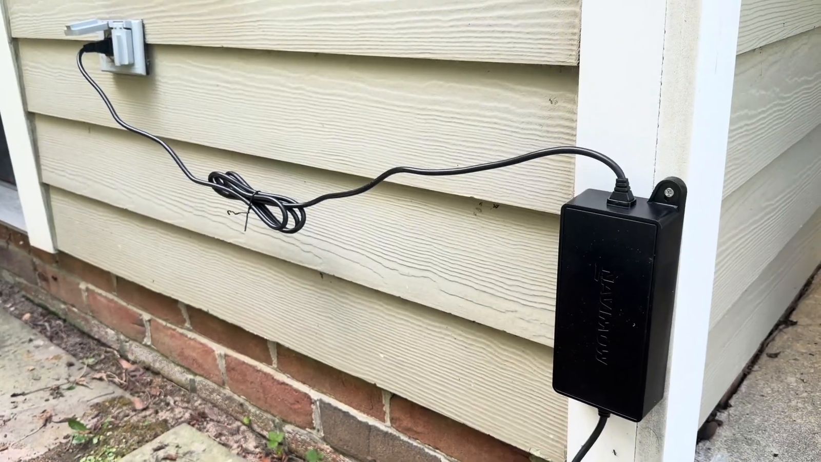 A Navimow power supply mounted off the ground on the house wall with the cable routed and secured