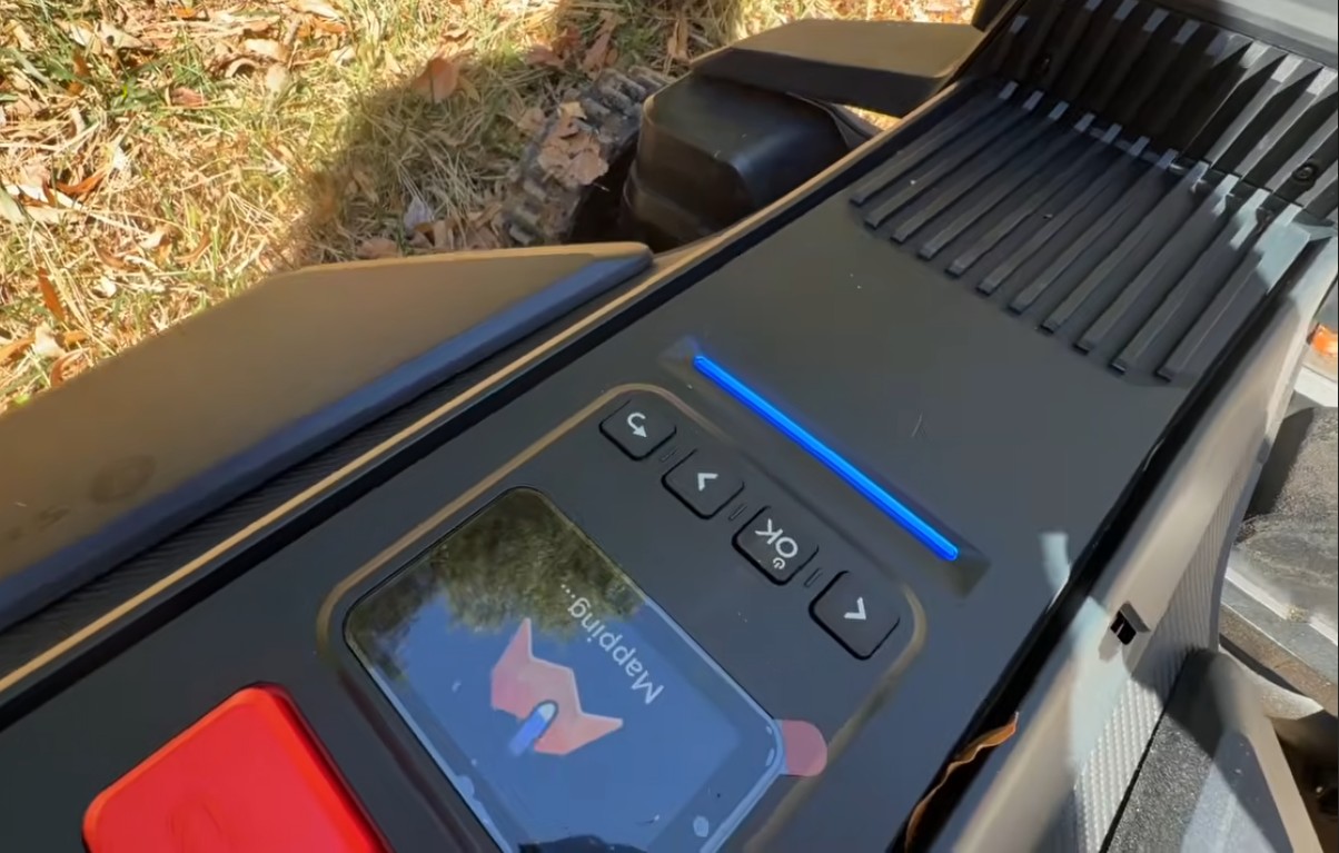 The control panel of a Navimow X430 on a leafy lawn, its light bar glowing solid blue while the display reads Mapping