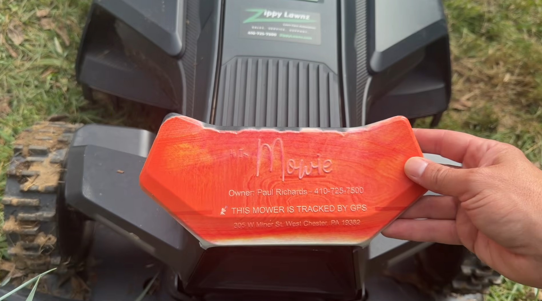A UV-printed owner ID plate on a Navimow X4 reading the owner's name and phone number and This Mower Is Tracked by GPS