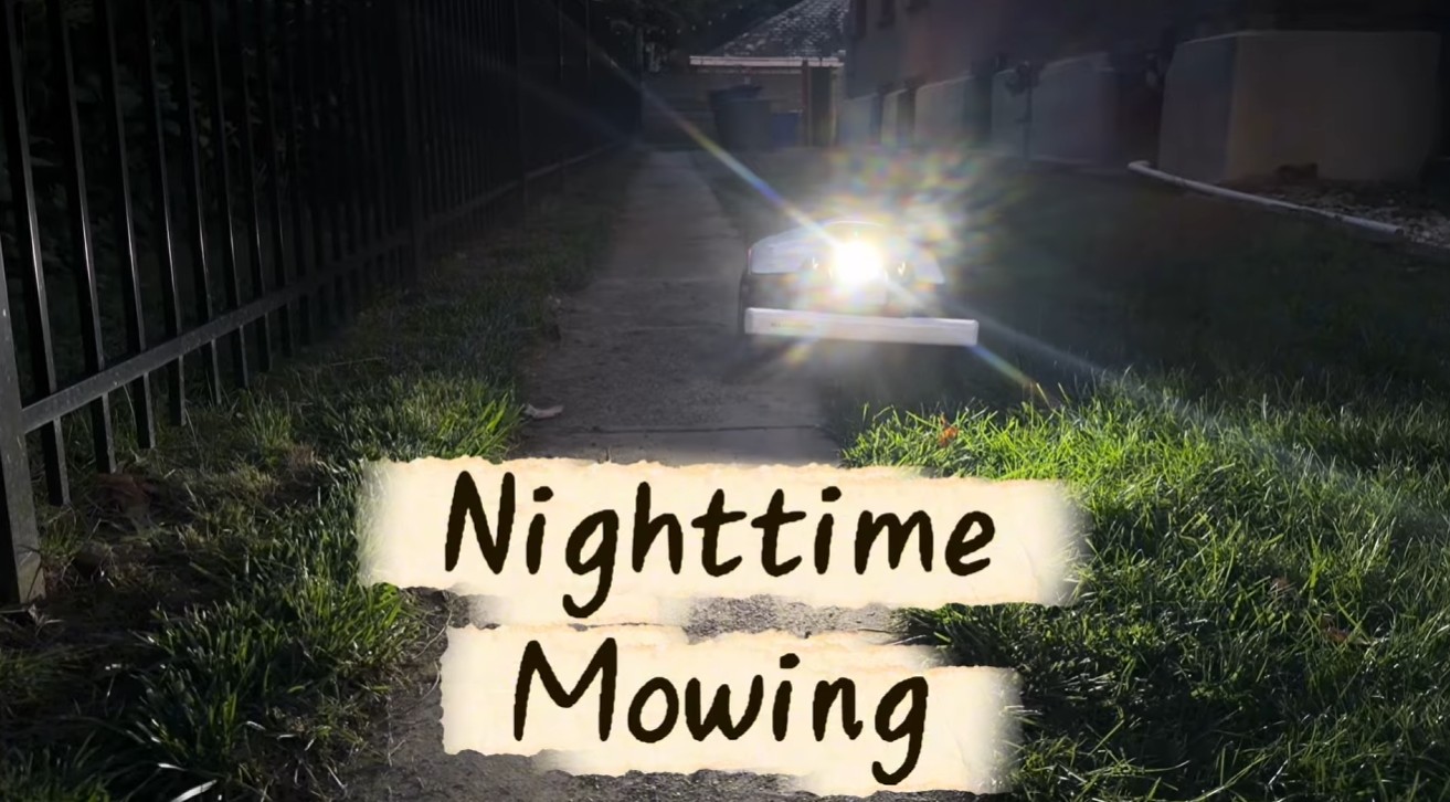 A robot mower mowing along a dark path at night with its headlight lit