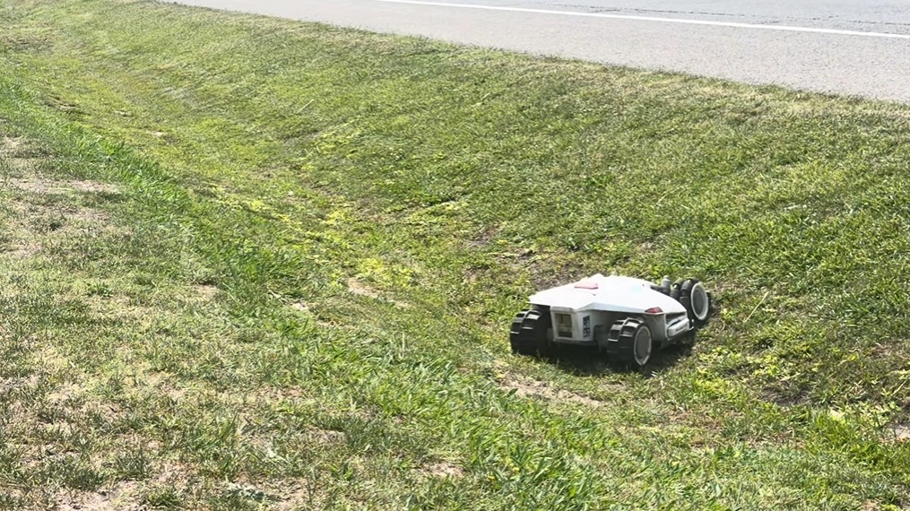 A robot mower cutting the grass in a roadside drainage ditch on a slope