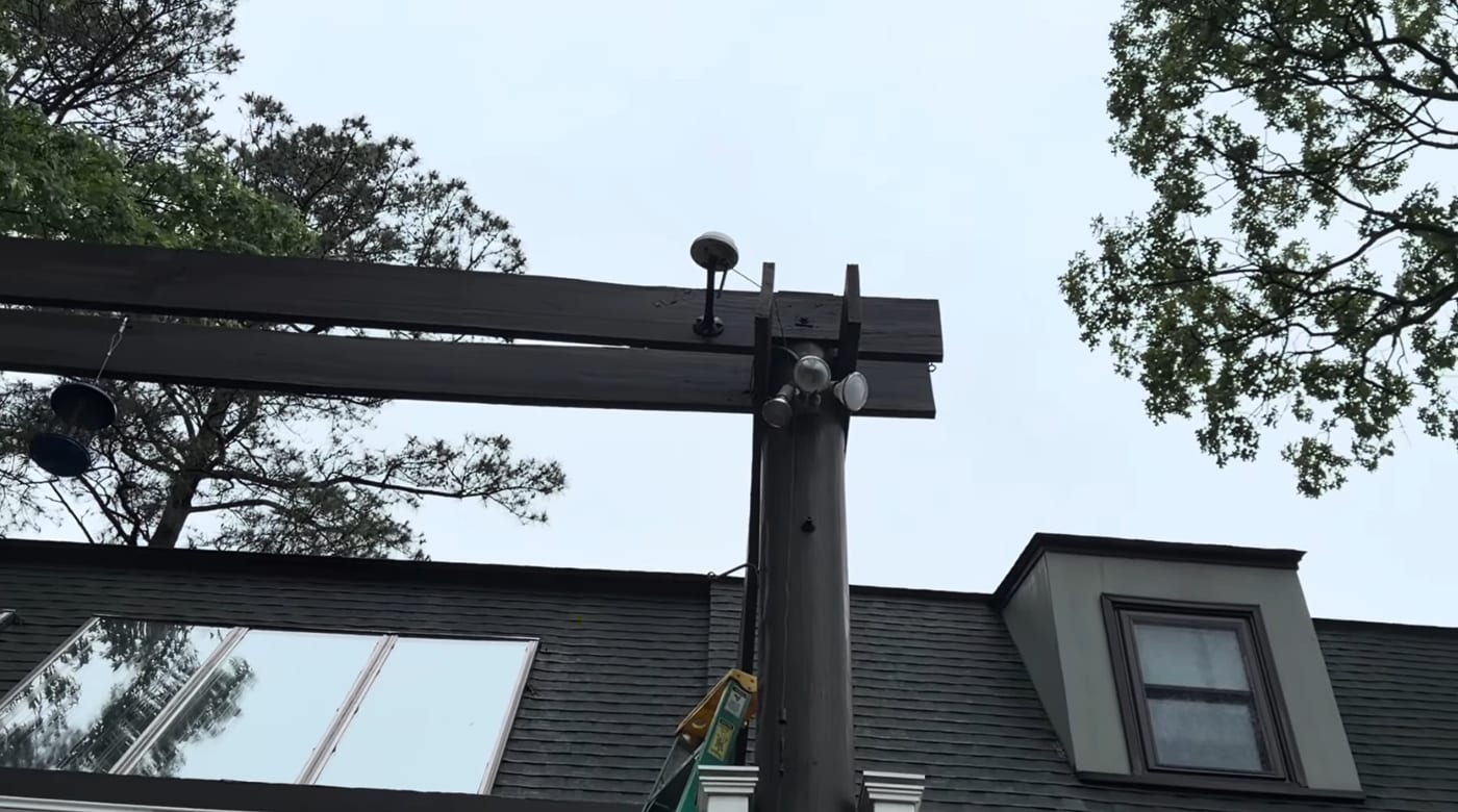 An RTK antenna mounted high on a pergola beam with clear open sky above it