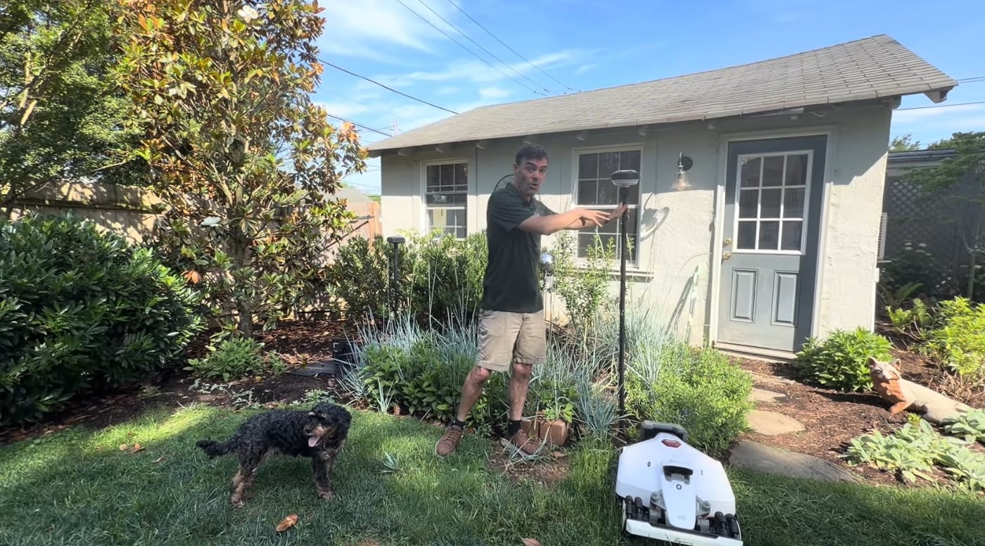 A dealer pointing to an RTK antenna mounted on a tall pole beside a robot mower and its dock