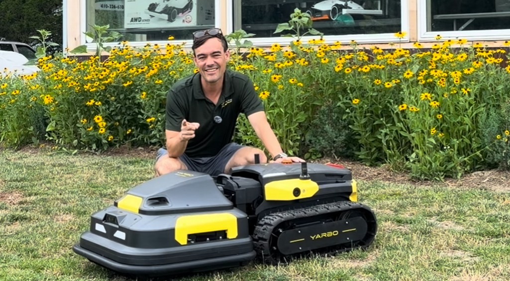 A tracked Yarbo robot mower cutting a clean border around a natural farm pond