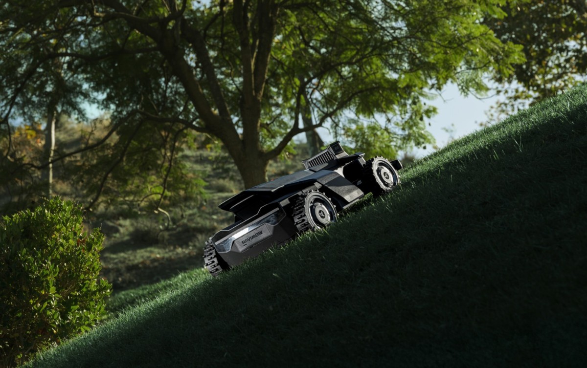 Segway Navimow robot mower cutting a steep grassy slope beneath mature trees