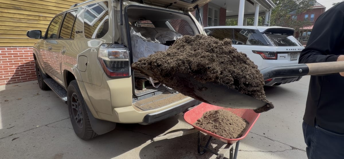 A shovel of dark compost coming out of the back of a car into a wheelbarrow