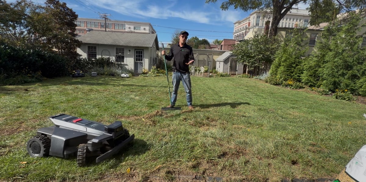 A raked, thin lawn with a robot mower and a bag of seed